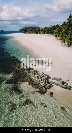 Vue aérienne d'une plage sereine aux Philippines avec des eaux turquoises claires et des palmiers luxuriants. Ce paradis tropical invitant capture les es Banque D'Images