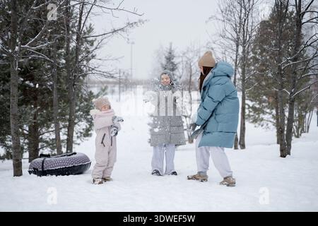 Une scène joyeuse d'une mère et de deux enfants jouant dans un parc enneigé pendant l'hiver. Les enfants sont emballés dans des vêtements chauds, leurs visages remplis de la Banque D'Images