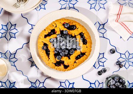 Un petit déjeuner appétissant composé d'une tarte dorée garnie de myrtilles fraîches et juteuses. Servi sur une table à motifs bleu et blanc, perfe Banque D'Images