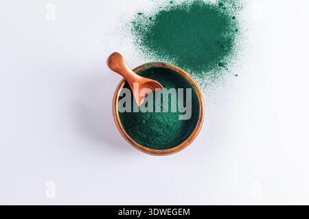 Vue de dessus de la poudre de spiruline verte vibrante dans un bol en bois avec une pelle en bois, sur un fond blanc immaculé. Parfait pour la santé et le bien-être Banque D'Images