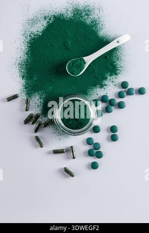 Vue de dessus de spiruline en poudre, capsules et comprimés sur une surface légère. Une cuillère blanche remplie de poudre de spiruline verte est placée à côté d'un bocal en verre Banque D'Images