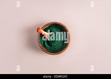 Vue de dessus de la poudre de spiruline verte vibrante dans un bol en bois avec une petite cuillère en bois, sur un fond rose pastel doux, parfait pour bio Banque D'Images
