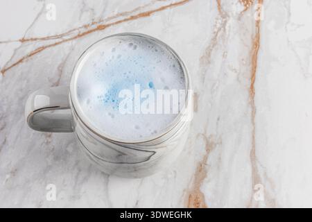 Un latte matcha bleu crème élégamment servi dans une tasse à motifs en marbre, placée sur une table en marbre poli. La touche bleue apaisante rehausse le peacefu Banque D'Images
