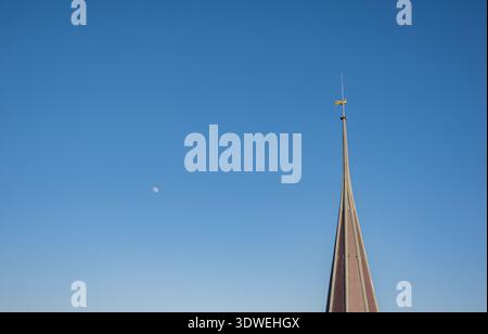 Une flèche d'église pointue à Lausanne s'étend vers le ciel. La demi-lune apparaît dans le fond bleu clair, mettant en valeur l'élégance architecturale et na Banque D'Images