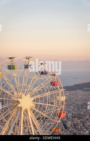 Une vue captivante de la grande roue sur Tibidabo contre l'horizon de Barcelone, magnifiquement éclairée par les teintes chaudes d'un coucher de soleil, créant un fascinant Banque D'Images