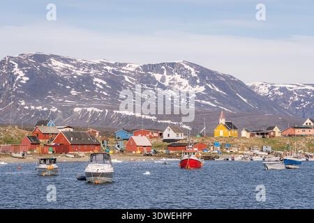 Vue panoramique sur le village de Saqqaq au Groenland, baigné par la lueur chaude du soleil de minuit. Des maisons colorées et des bateaux sont nichés contre la montagne accidentée Banque D'Images