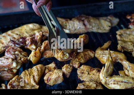 Gros plan de morceaux de poulet marinés grésillant sur un barbecue, présentant une texture juteuse et un riche assaisonnement tandis que les pinces tournent la viande pour l'extérieur Banque D'Images