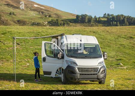 Une scène sereine de la vie de camping-car dans les Pyrénées, avec un van blanc confortable garé dans une prairie verdoyante avec un environnement montagneux, parfait pour Banque D'Images