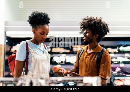 Un couple aime faire du shopping ensemble dans une épicerie. L'homme tient une tomate, s'engageant dans une conversation amicale avec la femme, pendant qu'ils explorent Banque D'Images