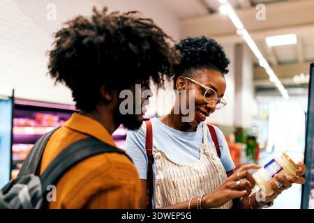 Un couple joyeux passant du temps ensemble tout en faisant du shopping dans un supermarché. La femme lit une étiquette, souriant comme l'homme regarde, entourée de St dynamique Banque D'Images