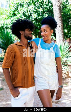 Heureux couple profitant d'une journée ensoleillée dans le parc, partageant sourires et compagnie. La femme s'appuie de manière ludique sur l'homme, mettant en valeur un naturel et joyeux Banque D'Images