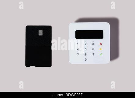 Une carte de crédit et un terminal de paiement élégant sont affichés sur un fond gris minimaliste. La carte est noire et le terminal comporte un clavier numérique Banque D'Images