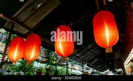 Des lanternes rouges brillantes sont suspendues sous une rue couverte de l'île de Hong Kong, créant une atmosphère chaleureuse et festive. Entouré de plantes et d'étals de marché, Banque D'Images