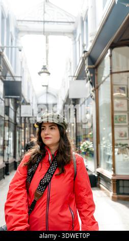 Une femme vêtue d'une veste et d'une casquette rouges se promène dans l'historique Morgan Arcade de Cardiff, au pays de Galles, entourée d'une architecture élégante et de boutiques, capt Banque D'Images