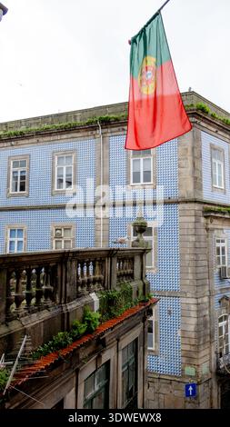 Un drapeau portugais flotte au-dessus d'un bâtiment historique avec des azulejos traditionnels à Vila Nova de Gaia, tandis qu'une mouette se perche sur la corniche. Banque D'Images