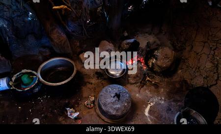 Intérieur de la cuisine d'une tribu Datoga en Tanzanie, avec un foyer ouvert entouré de pierres, de casseroles et d'ustensiles traditionnels, reflétant le ri Banque D'Images
