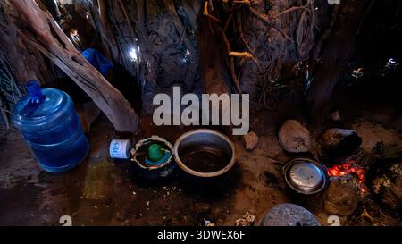 Intérieur de la cuisine d'une tribu Datoga en Tanzanie, avec un foyer ouvert entouré de pierres, de casseroles et d'ustensiles traditionnels, reflétant le ri Banque D'Images