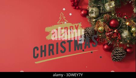 Avec la typographie JOYEUX NOËL associée à un groupe de couronnes sur une table rouge, des boules dorées Banque D'Images