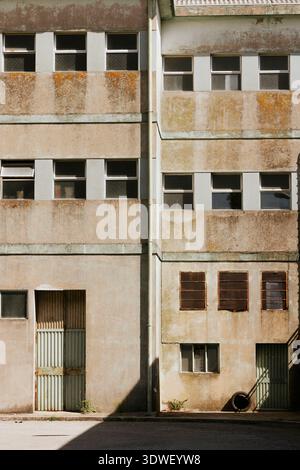 Un bâtiment industriel abandonné avec une façade usée et plusieurs fenêtres, capturant un extérieur sombre et altéré. La structure présente de la rouille et vi Banque D'Images