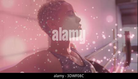 Femme debout portant un débardeur gris s'étendant près de barre dans le studio de danse, avec bokeh rose Banque D'Images