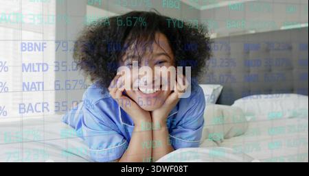 Femme mi-adulte souriante couchée sur le lit dans la chambre portant un haut de pyjama en satin bleu clair, superposition ticker Banque D'Images