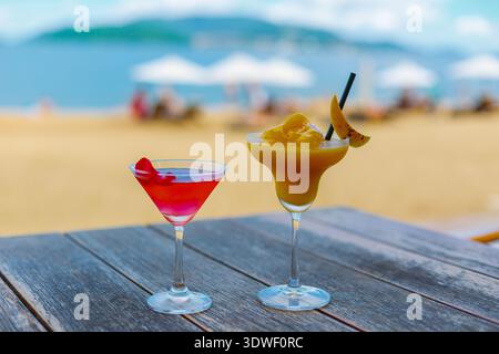 Deux cocktails vibrants assis sur une table en bois avec une plage pittoresque en toile de fond à Nha Trang, province de Khanh Hoa, Vietnam, capturant l'essence d'un parfait Banque D'Images