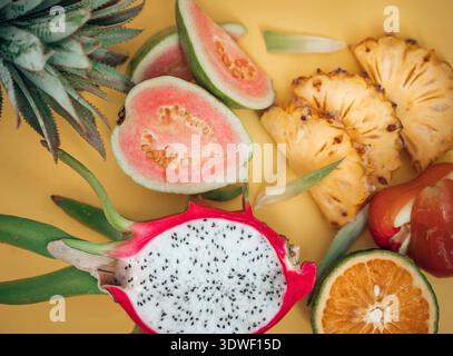 Un assortiment coloré de fruits exotiques et tropicaux, y compris goyave, ananas, fruit du dragon et tranches d'orange sur un fond jaune vif Banque D'Images