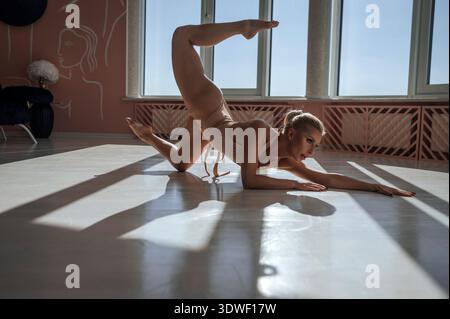 Une belle femme pratique le yoga dans un studio lumineux, en équilibrant gracieusement dans une pose basse. La lumière du soleil filtre à travers de grandes fenêtres, projetant profondément, frappant Banque D'Images