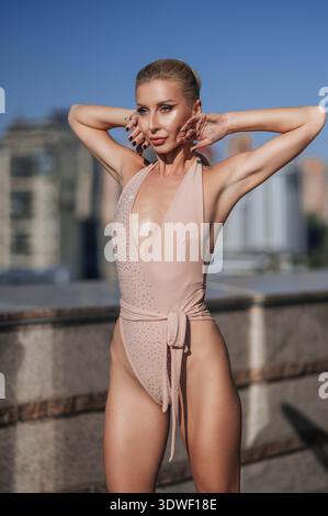 Une belle femme blonde pose en toute confiance dans un élégant léotard à l'extérieur. La lumière du soleil améliore sa forme physique, créant un i frappant et stimulant Banque D'Images