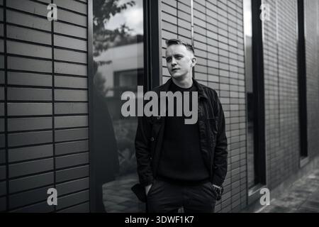 Portrait urbain en noir et blanc d'un jeune designer masculin à Kiev, Ukraine. Il se tient confiant contre un fond architectural moderne, réfléchissant Banque D'Images