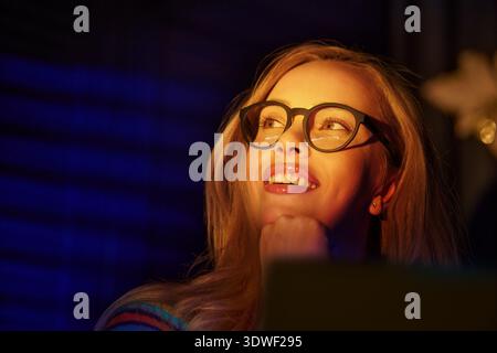 Femme blonde joyeuse utilisant un ordinateur portable et travaillant tard Banque D'Images