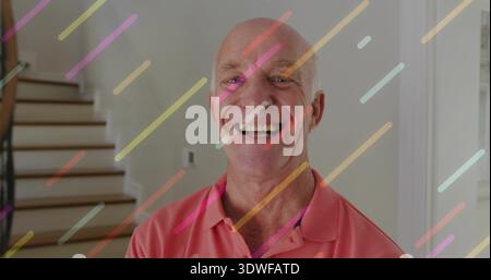 Homme âgé souriant portant un polo corail debout dans le hall, escaliers, étagères, interrupteur, rayures pastel Banque D'Images
