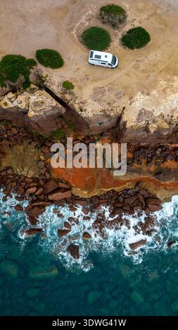 Vue aérienne de haut en bas d'un camping-car blanc garé sur le bord des falaises Macori à Calasetta. L'image met en évidence le contraste saisissant des couleurs entre Banque D'Images