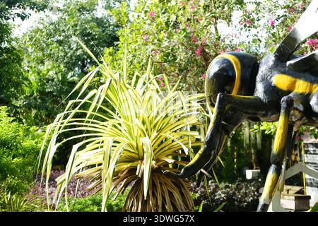 Vue rapprochée d'un modèle d'abeille avec des rayures jaunes et noires vives, sur fond de plantes tropicales et de verdure dans un jardin Banque D'Images