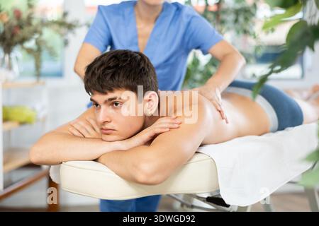 Masseur féminin faisant le massage à l'homme de dos qui couché sur la table de massage dans le salon de beauté Banque D'Images