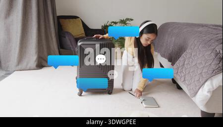 Femme adulte agenouillée atteignant la poignée de la valise sur le sol de la chambre, portant le dessus jaune et des écouteurs Banque D'Images