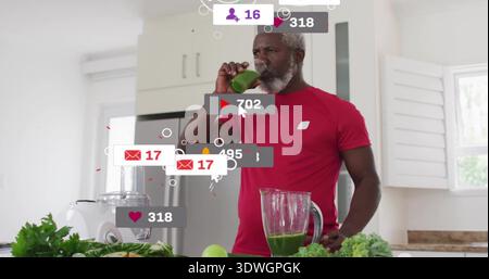 T-shirt rouge pour homme buvant un smoothie vert en verre transparent au comptoir de la maison avec superposition du mélangeur Banque D'Images