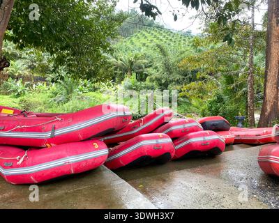 Bateaux de rafting empilés aux couleurs vives reposant sur une zone bétonnée, entourée de verdure et de collines, préparés pour des excursions touristiques Banque D'Images