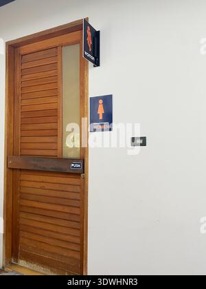 Porte de toilettes en bois étiquetée pour les femmes, avec un panneau à pousser et un symbole de figure féminine, serrée contre un mur blanc dans un espace public Banque D'Images