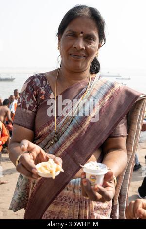 Portrait d'une femme indienne dans le saree traditionnel offrant de la nourriture près de la rivière à Varanasi, Inde. Banque D'Images