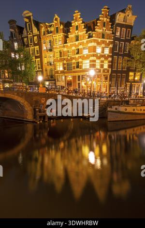 Pays-Bas. Nuit sur le canal d'Amsterdam. Dansant des maisons hollandaises avec des lumières. Bar avec tables extérieures. Vieux bateau amarré Banque D'Images