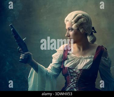 Une femme se tient debout dans une pièce faiblement éclairée, vêtue de vêtements historiques. Elle tient un pistolet et regarde soigneusement sur le côté alors que la fumée monte autour d'elle. Banque D'Images