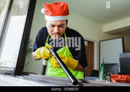 Équipe de nettoyage asiatique professionnelle en uniformes festifs fournissant un service de nettoyage de Noël, préparant la maison et le bureau pour la célébration des fêtes. Banque D'Images