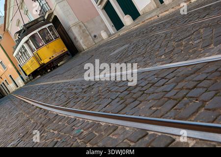 Plan grand angle bas des voies de tramway sur une rue pavée escarpée avec un tramway jaune en arrière-plan, Alfama, Lisbonne, Portugal, Europe. Banque D'Images