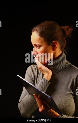 Femme d'affaires dans un cadre moderne sombre tenant un appareil numérique, soulignant l'accent professionnel, l'utilisation de la technologie contemporaine, flux de travail productif et Banque D'Images