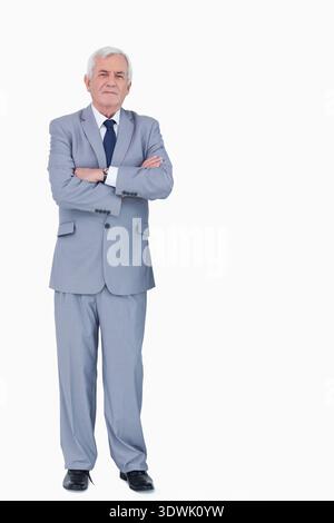 Bras debout masculin senior croisés portant costume, cravate marine, montre, chaussures noires en studio, espace copie. Aîné, homme, formel, veste, pantalon, cravate tim Banque D'Images