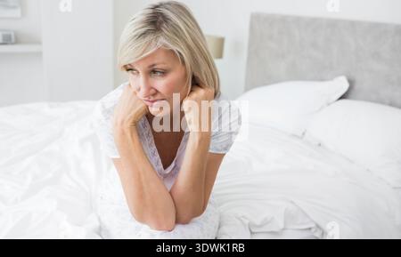 Femme mature assise sur le bord du lit dans la chambre portant un haut de pyjama léger, tenant le cou. Contemplation, style de vie, minimal, maison, privé, oreillers, tête Banque D'Images