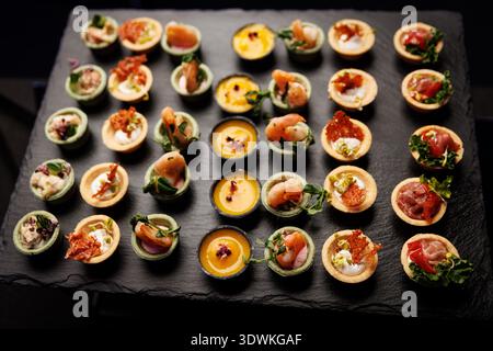 Une variété de petites tartes salées et canapés disposés en rangées pour un événement. La sélection comprend des crevettes, de la mousse et des garnitures de légumes. Banque D'Images