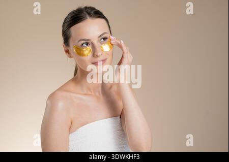 Femme appliquant des patchs dorés sous les yeux pour les soins de la peau et le rajeunissement Banque D'Images