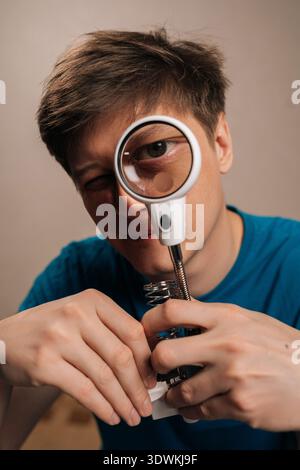 Portrait vertical du technicien se concentrant à travers une loupe avec lumière intégrée, inspectant les fils et les composants sur un petit appareil, engagé dans Banque D'Images